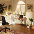 Modern black and walnut office desk with slim steel legs in a bright home workspace with plants and ergonomic chair
