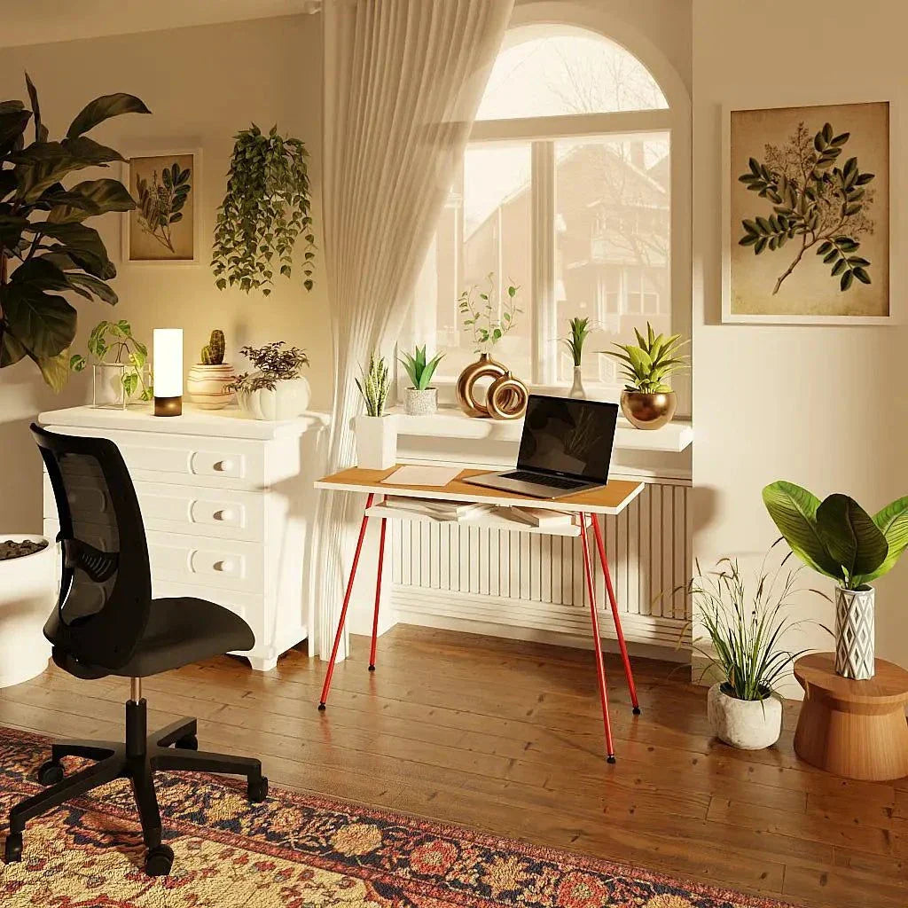 Compact red and chocolate cherry office desk with laptop on top, positioned in a bright home office setting with plants and ergonomic black chair.
