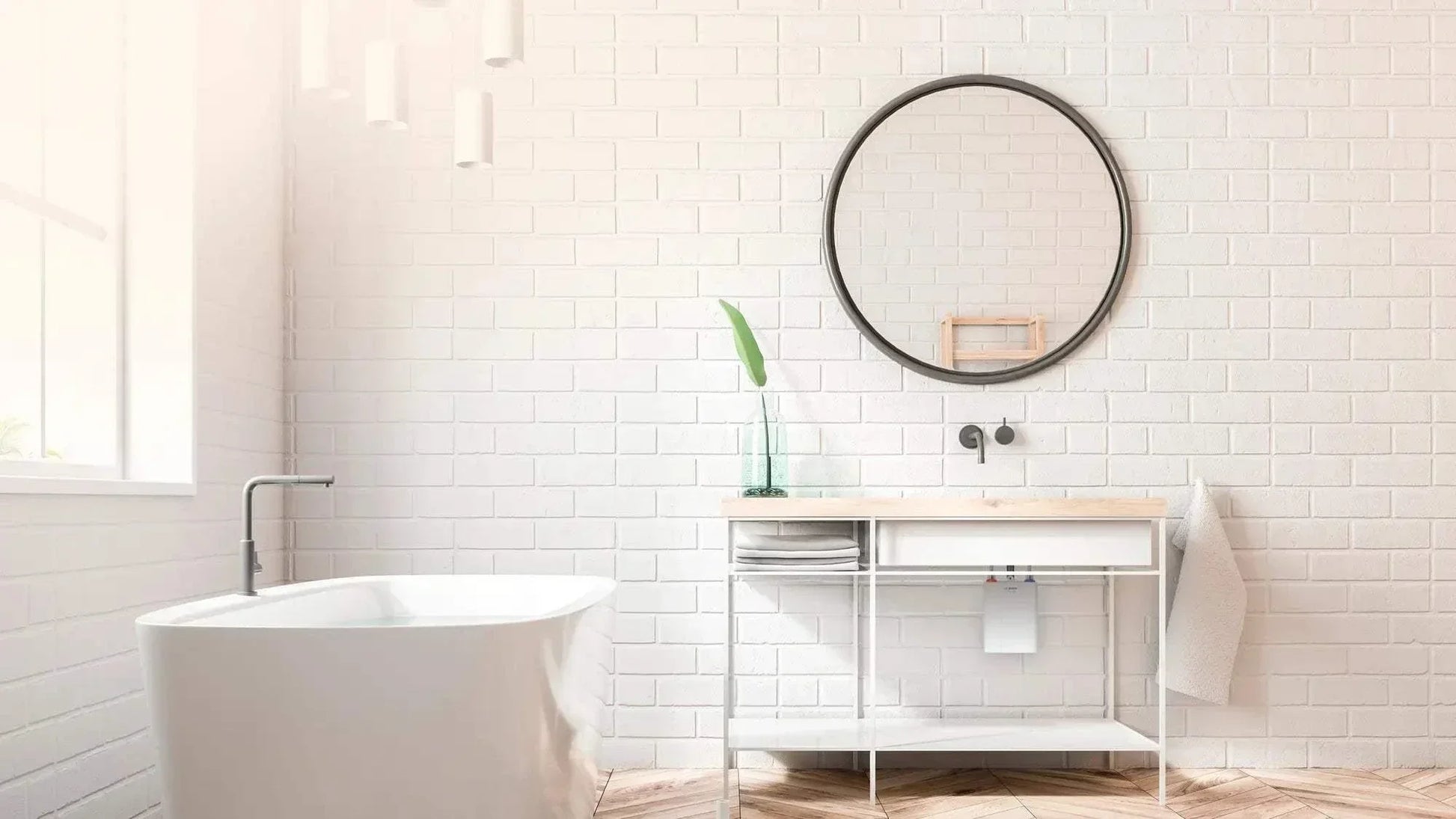 Compact electronic instant water heater Bosch Tronic 4000 6 EB installed in modern white bathroom with round mirror and freestanding bathtub.